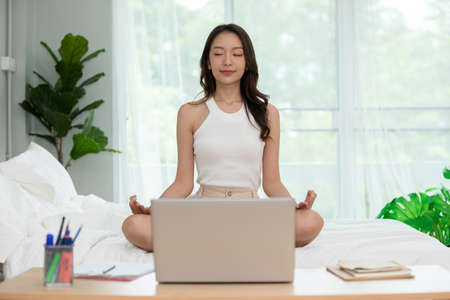 Athlete Asian woman looking laptop practice yoga lotus pose online course at home to meditation comfortable and relax,yoga Exercise at home Concept,Self isolation due COVID-19 pandemicの写真素材