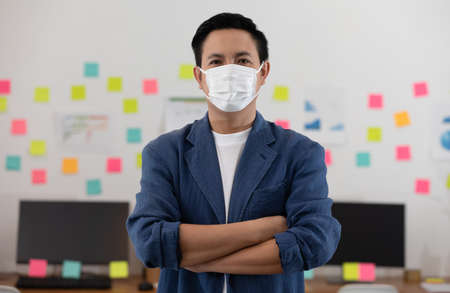 Asian senior business man in casual wearing mask Standing cross arms in modern office or co-working...