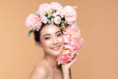 Beauty Asian young woman with big bouquet flowers on head smile with clean fresh skin Happiness and cheerful with positive emotional on Beige background,Beauty Cosmetics and Facial treatment Conceptの写真素材