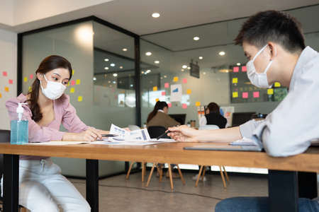 Business man and woman wearing face mask meeting and working together for discussion and brainstrom to get ideas or marketing solution with social distance due COVID-19 virus flu pandemic and protectの写真素材