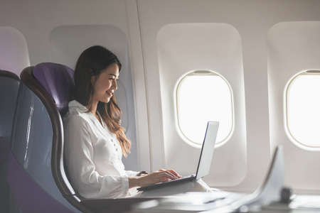Asian young woman using laptop sitting near windows at first class on airplane during flight,Traveling and Business conceptの写真素材