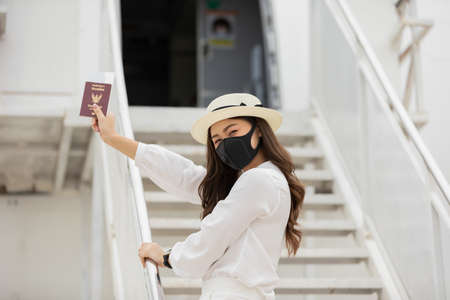 New normal of Asian young woman wearing protective mask holding passport ready to trevel at airplane,Traveling and Business during COVID-19 virus pandemic conceptの写真素材