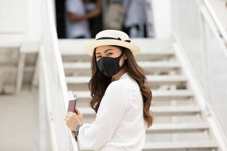 New normal of Asian young woman wearing protective mask holding passport ready to trevel at airplane,Traveling and Business during COVID-19 virus pandemic conceptの写真素材
