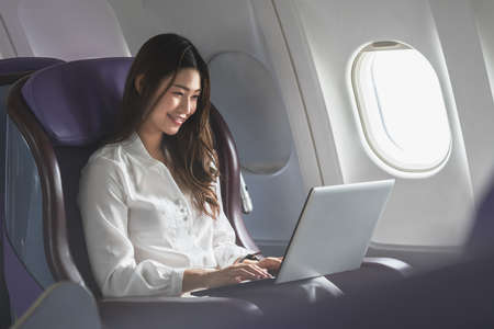 Asian young woman using laptop sitting near windows at first class on airplane during flight,Traveling and Business conceptの写真素材