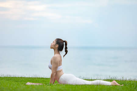 Athletic Asian young woman practice Cobra Pose on green grass and beach in Tropical island,Feeling...