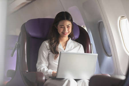 Asian young woman using laptop sitting near windows at first class on airplane during flight,Traveling and Business conceptの写真素材