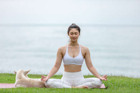 Asian young woman practice yoga lotus pose to meditation with dog on the beach feeling so happiness and cheerful,Travel in tropical beach in Thailand,vacations and relaxation Concept