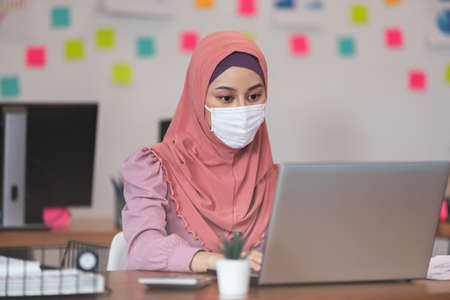 New normal of Asian business Muslim or islam women wearing face protective mask in casual working with laptop and smile looking at camera at modern office or Co-Working Space,Business Startup Conceptの写真素材