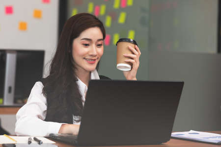 Happy Asian business woman in casual working with laptop and smile looking at camera at modern office or Co-Working Space,Business Startup Conceptの写真素材