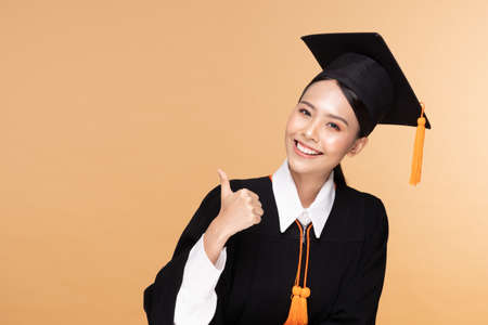 Beautiful Attractive Asian woman graduated in cap and gown smile so proud and happiness,Isolated on Beige background,Education Success Conceptの写真素材