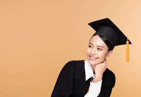 Beautiful Attractive Asian woman graduated in cap and gown smile so proud and happiness,Isolated on Beige background,Education Success Conceptの写真素材