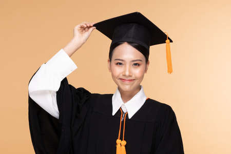 Beautiful Attractive Asian woman graduated in cap and gown smile so proud and happiness,Isolated on Beige background,Education Success Conceptの写真素材