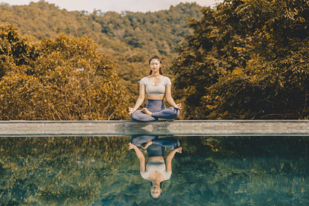 Calm of Beautiful Attractive Asian woman practice yoga Lotus pose on the pool above the Mountain peak in the morning in front of beautiful nature views,Feel so comfortable and relax in holidayの写真素材