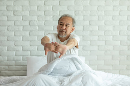Elderly asian man stretching arm after wake up on bed and looking outside windows in bedroom feeling so fresh and relax in the morning,Healthcare Conceptの写真素材
