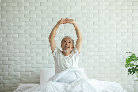 Elderly asian man stretching arm after wake up on bed and looking outside windows in bedroom feeling so fresh and relax in the morning,Healthcare Conceptの写真素材