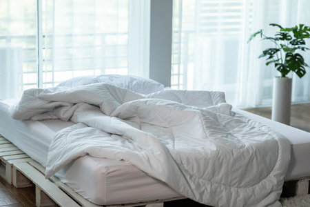Messed bed with white pillow and duvet blanket with natural light in bedroom in the morning,Messy...