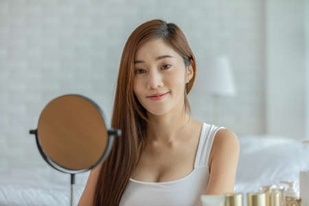Happy Asian young woman smile and looking in camera doing skin care and beauty treatment at home,Wellness woman self care with beauty product at homeの写真素材