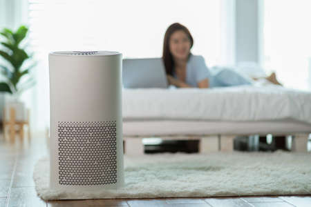 air purifier in bed room for clean dust and fresh air with woman lying on bed working with computer laptop and relax in background,Wellness of clean and fresh air for breathing and good health at homeの写真素材