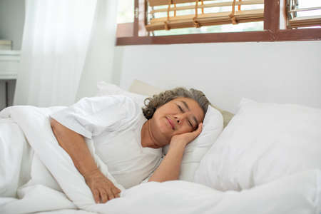 Asian Elderly woman with white hairs close eyes smile sleep and sweet dream on bed in cozy bedroom in the morning feeling so relax and comfortable,Healthcare and Sleep Conceptの写真素材