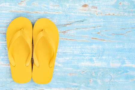 top view of yellow slippers on blue wooden background,Flat lay of summer vacation and travel conceptの写真素材