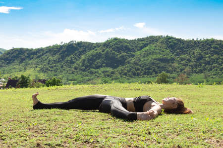 Asian woman practice yoga Supta Padangustasana B or Reclining Hand to Big Toe Pose stretching exercise muscle with yoga meditation relax and refresh health on green grass feeling happinessの写真素材