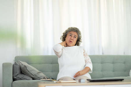 Asian Elderly senior woman with white hairs neck and shoulder pain and illness on sofa alone at...