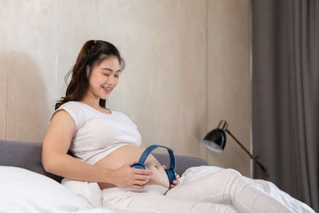 Young Attractive Asian pregnant woman listen music and lying on bed.Pregnant woman use headphones to play classical music for baby in belly learn and Development feeling so relax,Pregnancy Conceptの写真素材