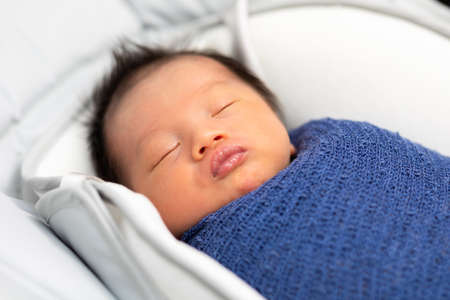 Adorable sleeping newborn baby relax in a blue stretch wrap material on baby bed.Asian newborn...