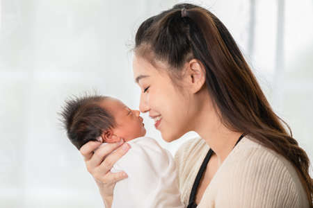 Beautiful Attractive Asian mom holding her baby newborn in hand and kissing on baby nose sweet and lovely.Happy mother and infant baby looking together smile with love.Mother and baby newborn Conceptの写真素材