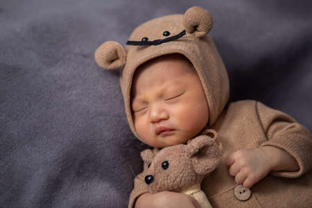 happy newborn baby weaing cute Mouse costume lying sleeps and hug doll on Beige background...