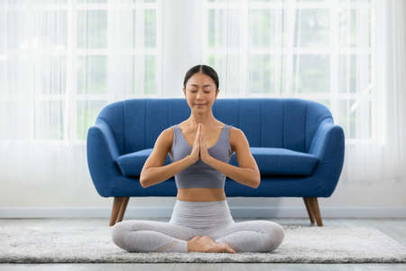 Calm of wellness Asian young woman sit on carpet breathing with yoga lotus pose,Yoga meditation of young healthy woman relax and comfortable at white cozy home,Yoga Exercise for Wellness Conceptの写真素材