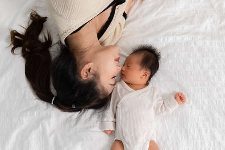 Top view of Beautiful Attractive Asian mom lying on bed kissing on baby sweet and lovely.Happy mother and infant baby looking together smile with love.Mother and baby newborn Conceptの写真素材
