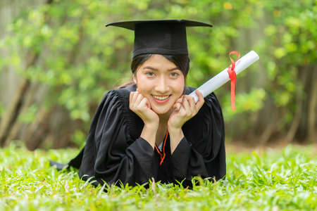 Attractive Asian Women Student Graduate in cap and gown celebrating with certificate in hand and so...