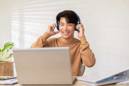 Entrepreneur handsome business asian man wear casual shirt and earphone listen having fun with music.Happy freelance wear wireless headphones dancing on desk at home during take a breakの写真素材