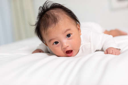 Newborn baby 3 month laying on stomach developing neck control .tummy time for strengthen baby neck and shoulder muscles.Cute infant lying crawling on white bed happiness and fun.Tummy Time Conceptの写真素材