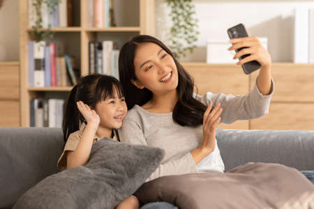Asian young mother and her daughter have video call conference with family having fun...