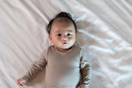 Top view happy newborn baby lying on a white bed and blanket comfortable and safety.Cute Asian...