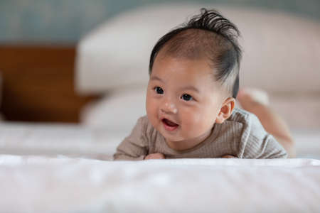 Newborn baby 4 month laying on stomach developing neck control .tummy time for strengthen baby neck and shoulder muscles.Cute infant lying crawling on white bed happiness and fun.Tummy Time Conceptの写真素材