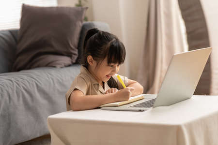 Little Asian girl child study online learn on laptop at home smile and happiness.Cute girl drawing...