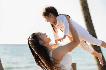 Happy asian mom holding her daughter playing together on the beach with fresh air.happy outdoor little girl hugging mother smile and love having fun enjoy with sunset on the beach.Mother day conceptの写真素材