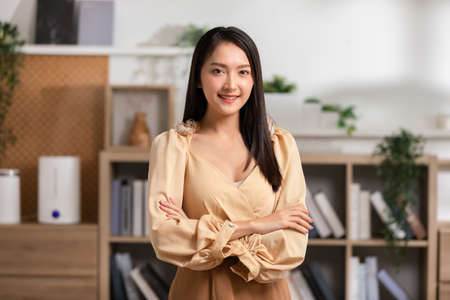 Stunning Beautiful Attractive Asian young woman standing looking at camera and smile happiness and comfortable at home.Cute girl smile cross arm confident and relax in living room at homeの写真素材