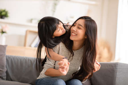 Fun mom with cute baby girl. Mother and daughter playing together in the living room. Asian girl...