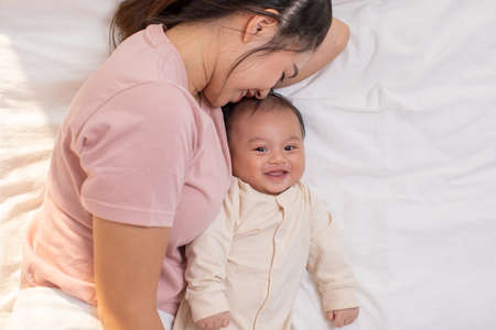 Mom and kid are laying down and cuddling. Mom is kissing her son and both are smiling. Cute baby boy...