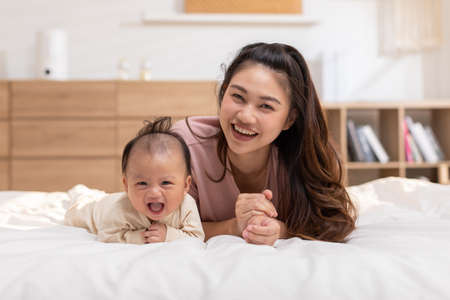 New asian mom Newborn baby laying on stomach developing neck control.tummy time for strengthen baby neck and shoulder muscles.Cute infant lying crawling with mother happy and fun.Tummy Time Conceptの写真素材