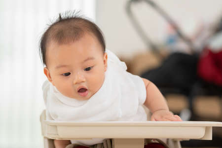 Asian baby sit on chair and looking down to view something amazed and excite be all around.Adorable baby boy cheerful enjoy with good moment in warmth place.growth with good Emotional Quotientの写真素材