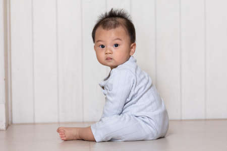 Healthy asian baby toddler sitting on floor to learn to crawl indoors looking at camera. Adorable...