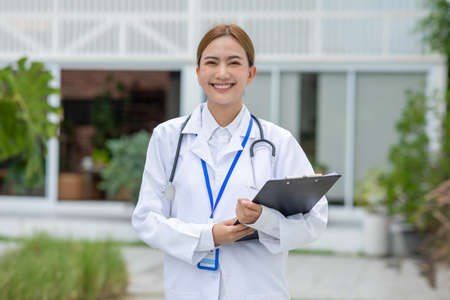 Asian female doctor with a stethoscope smile looking at camera. Doctor woman wear white coat smile with heartwarming comfortable.Positive emotional and good moment.Health Care Conceptの写真素材