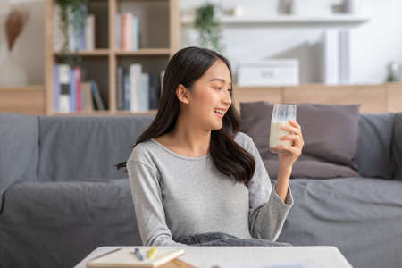 Healthy Young Asian woman Drinking milk with calcium for strong bone at home. Smiling indian woman holding soy milk on glass enjoy with nutrition wellness life.Wellness with natural milk fresh Conceptの写真素材