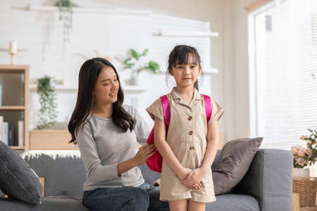 Asian mother preparing school bag of her daughter ready to school in morning. Happy mom helping her little girl get ready for school with love. First day to school. Good moment family.の写真素材