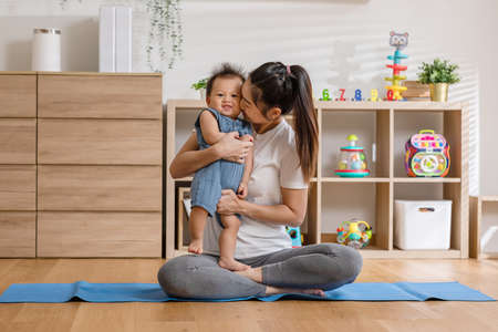 Happy Asian mom kissing her newborn baby smile and spending time for good moment together at warmth place. Adorable little baby boy having fun and cheerful with love from mother.Mother day conceptの写真素材